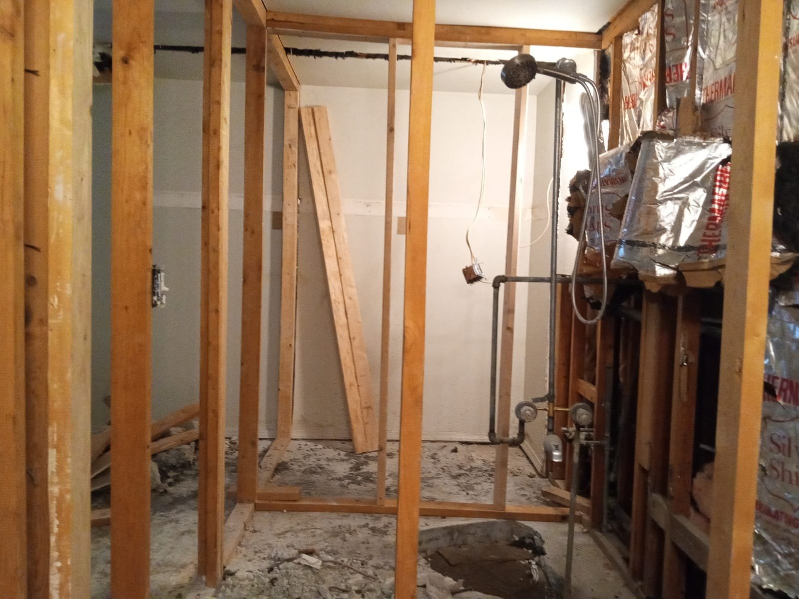 Bathroom remodel in progress with exposed framing, plumbing pipes, and shower installation